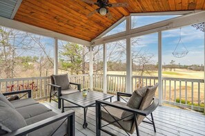 Ein überdachter Außenbereich mit Tisch und Stühlen, einem Deckenventilator und Blick auf einen Golfplatz.
