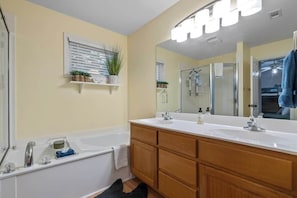 Un baño con bañera, tocador doble, armarios de madera, un espejo grande y zona de ducha.