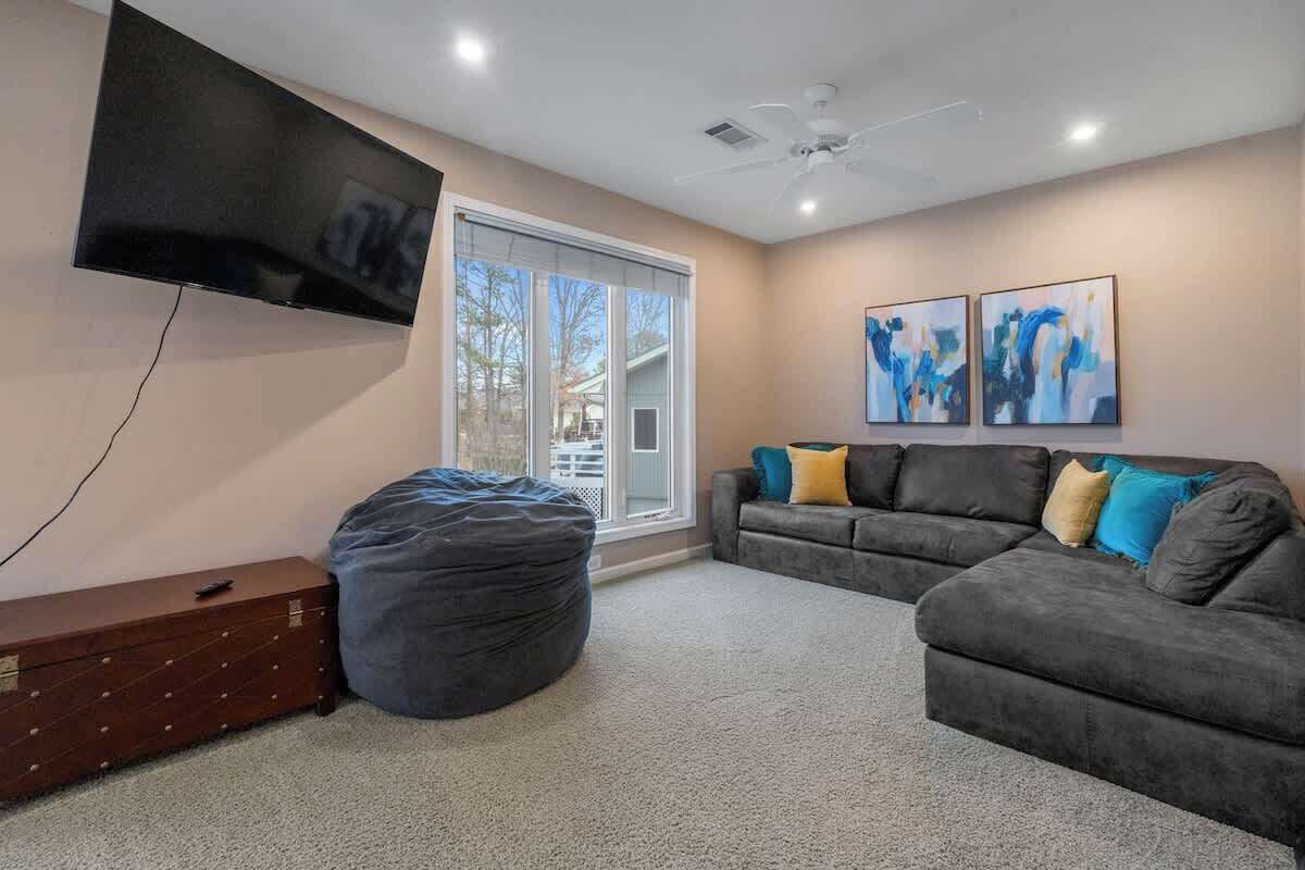 Una sala de estar con un televisor de pantalla plana, un sofá gris, un sillón orejero y dos cuadros abstractos en la pared.