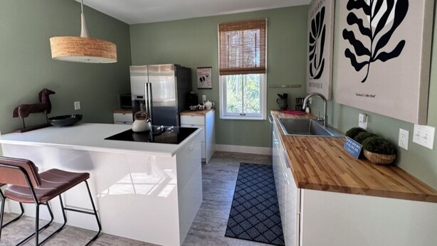 Una cocina moderna con una isla central, encimera de madera y una lámpara colgante.