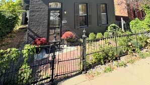 Una casa de dos pisos con fachada de piedra, una entrada principal con puerta y ventana, y un pequeño jardín con cerca.
