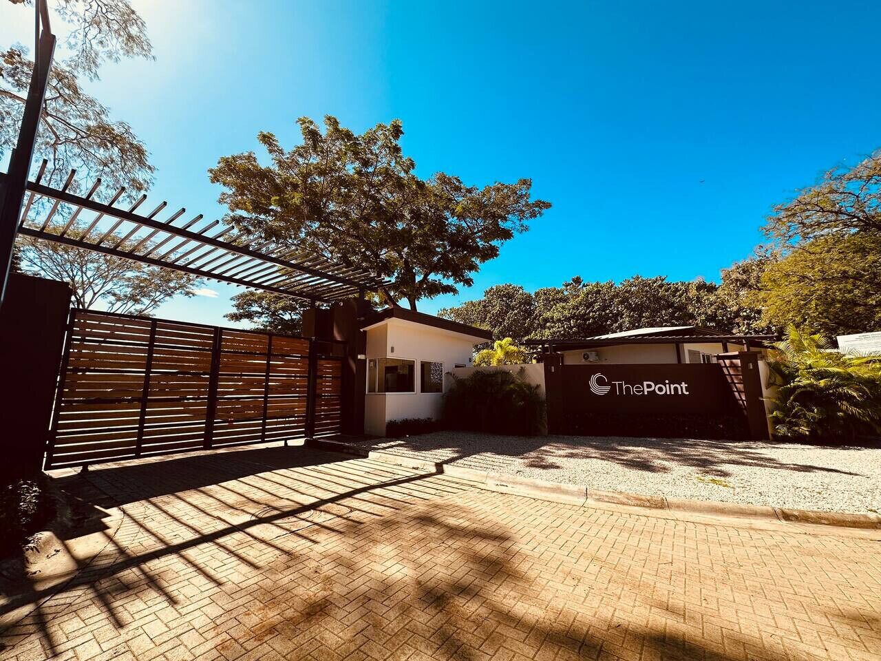 A gated entrance with a sign reading "The Point," a paved driveway, and a building with a modern design.