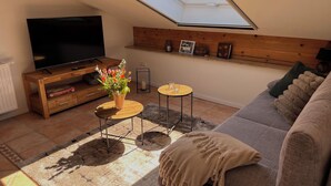 A living room with a TV, wooden shelves, a skylight, a sofa, and a small table.