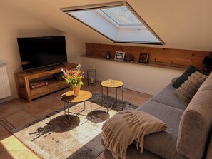 A living room with a TV, wooden shelves, a skylight, a sofa, and a small table.
