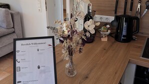 A modern kitchen with a wooden countertop, a vase with dried flowers, a coffee maker, and a framed welcome sign.