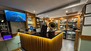 A bar area with a wooden counter, a vintage gramophone, and a television displaying a mountain view.