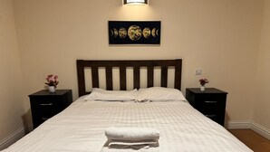 A neatly made bed with a checkered bedspread, two bedside tables with lamps, and a wall-mounted artwork depicting the moon phases.