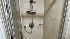 A glass-enclosed shower stall with a handheld showerhead, a wall-mounted faucet, and a small shelf.