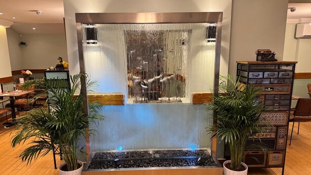 A modern indoor waterfall feature with a metal basin and two potted plants.