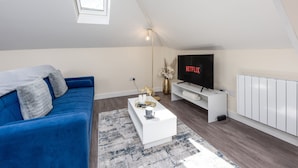 Un salon moderne avec un canapé bleu, une table basse blanche et un téléviseur affichant le logo « NETFLIX ».