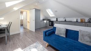 Un appartement moderne de style «loft» comprenant un coin repas, un canapé bleu et une cuisine dotée d’une verrière.