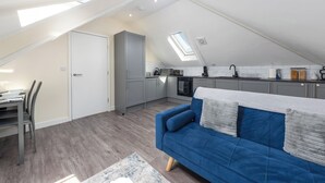 Un appartement de style loft comprenant un coin repas, une kitchenette, un canapé bleu et une lucarne.