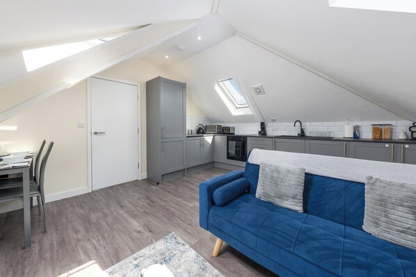 Un apartamento estilo loft con comedor, kitchenette, sofá azul y tragaluz.