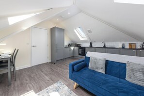 Un apartamento estilo loft con comedor, kitchenette, sofá azul y tragaluz.