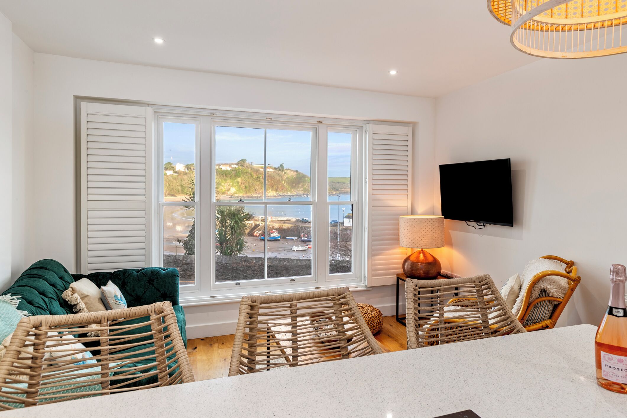A room with a large window, wicker chairs, a TV, and a bottle on the counter.