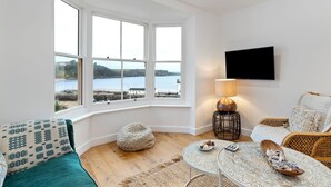 A cozy living room with a view of the sea, a television mounted on the wall, and a comfortable seating area.