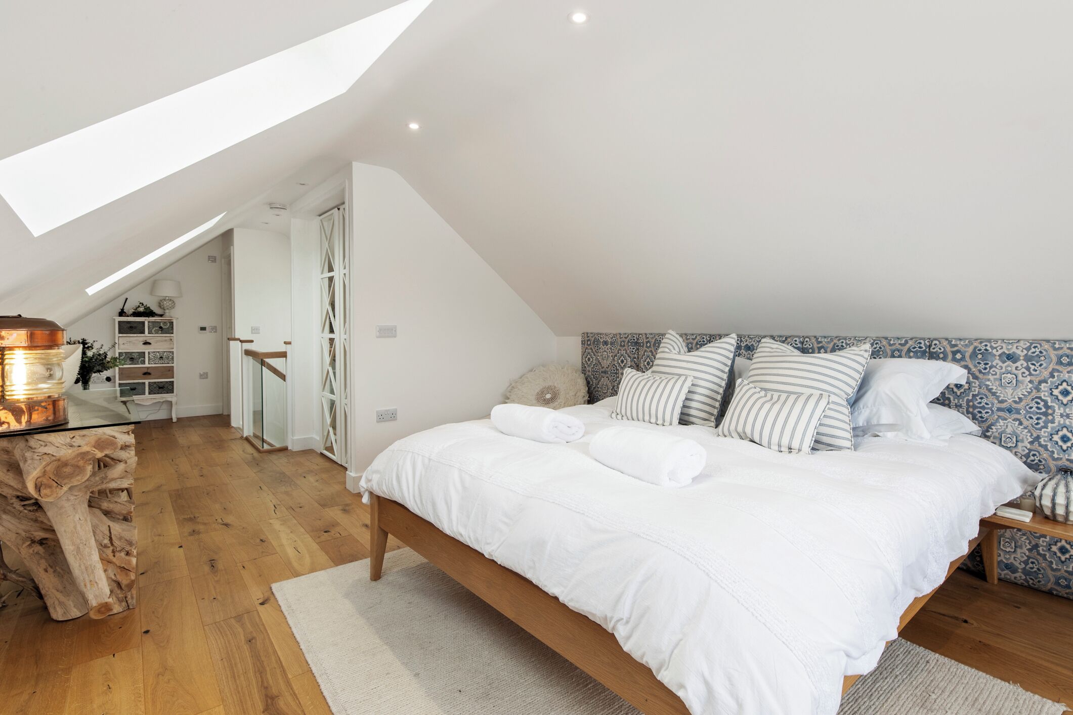 Une chambre avec un plafond en pente, un lit en bois, une tête de lit à motifs et un puits de lumière.