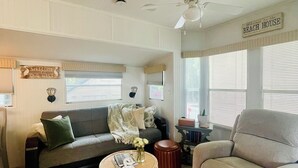 A spacious living room with a grey sofa, a round coffee table, and a beige armchair. There is a ceiling fan, a sign reading "Welcome to the Beach House," and a window with blinds. - The Newly Renovated  Couples  Retreat in Key Largo , Pool  beach , and Marina  (Key Largo)