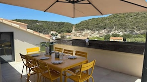 A dining area with a table and chairs, an umbrella, and a view of a hillside with buildings. - On the marina, superb 150m2 / 1,600 sq ft, with 2 terraces, A/C, parking & lift (Bonifacio)