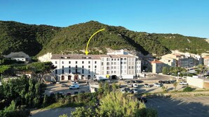 Edifici amb un pati central, envoltat de cotxes aparcats i vegetació.