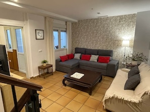A living room with a grey sectional sofa, a coffee table, a TV, and a patterned wallpaper.