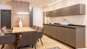 A modern kitchen with a wooden dining table, grey chairs, and a built-in oven. - Premium Suite With Private Sauna (Saalbach-Hinterglemm)