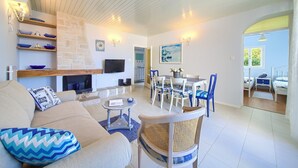 A spacious living room with a fireplace, a dining area with blue chairs, and a view of the outdoors. - Villa Sea Bound with Pool (Malinska)