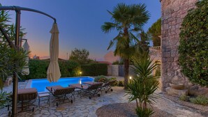 A stone patio with a swimming pool, lounge chairs, and a pergola with an umbrella. - Villa Sea Bound with Pool (Malinska)