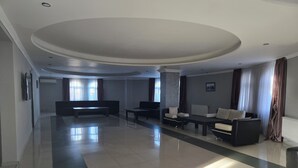 A spacious, modern living room with a large sofa, a coffee table, and a TV. The room has a high ceiling and large windows with curtains. - Kale Park  (Batumi)