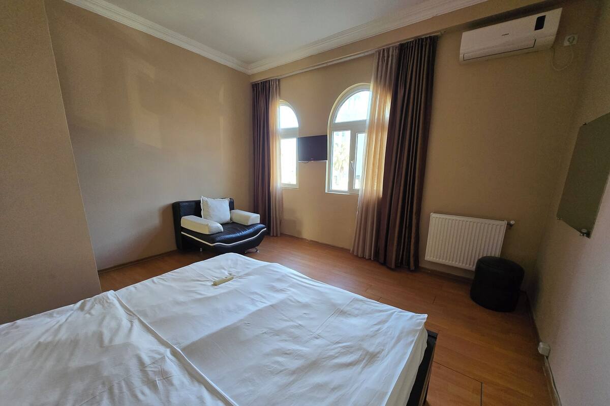 Ein Hotelzimmer mit einem großen Bett, einem Sessel, einem Fenster mit Vorhängen und einer Klimaanlage.