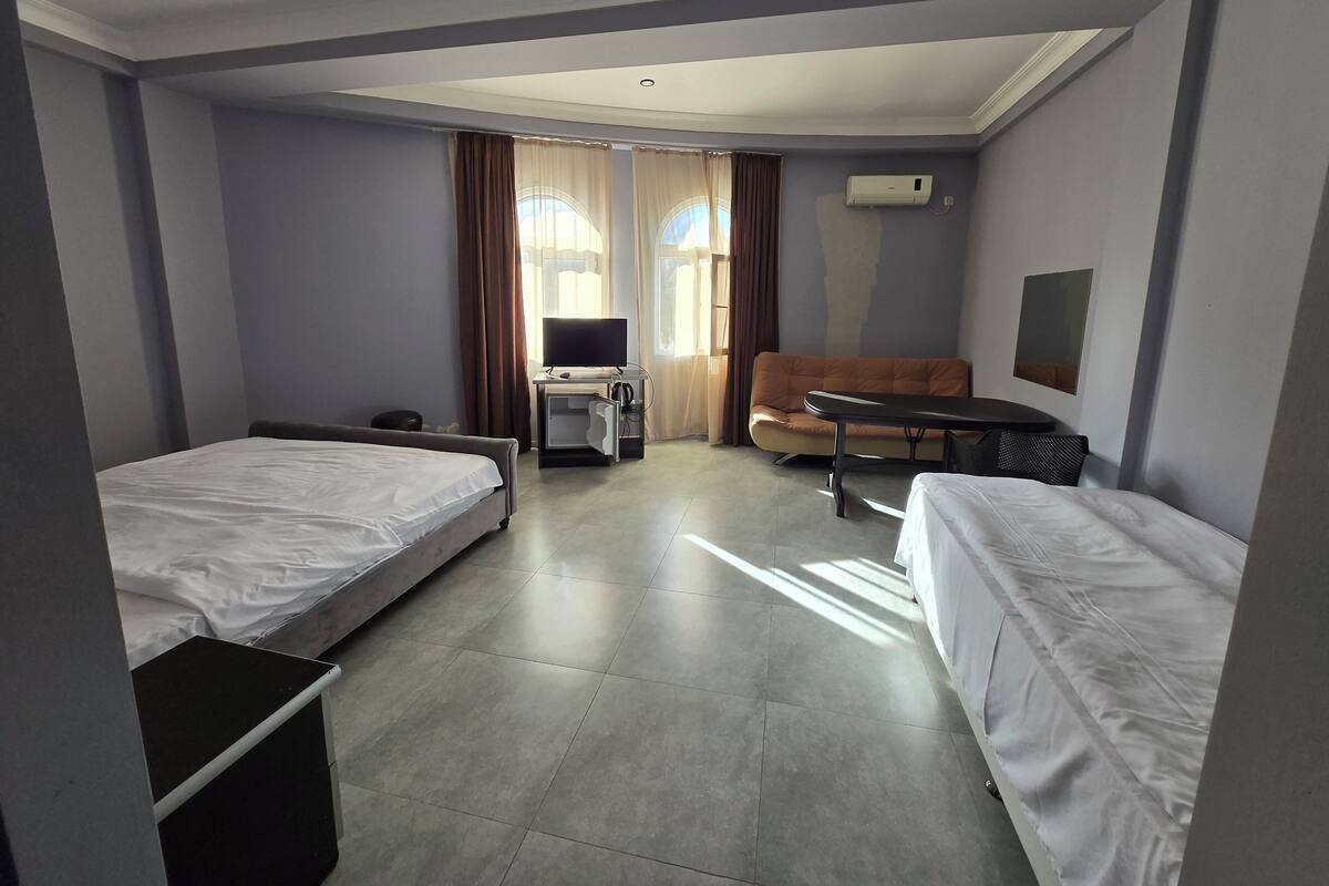 Ein Hotelzimmer mit zwei Einzelbetten, einem Schlafsofa, einem Schreibtisch mit Computer und einem Fernseher.