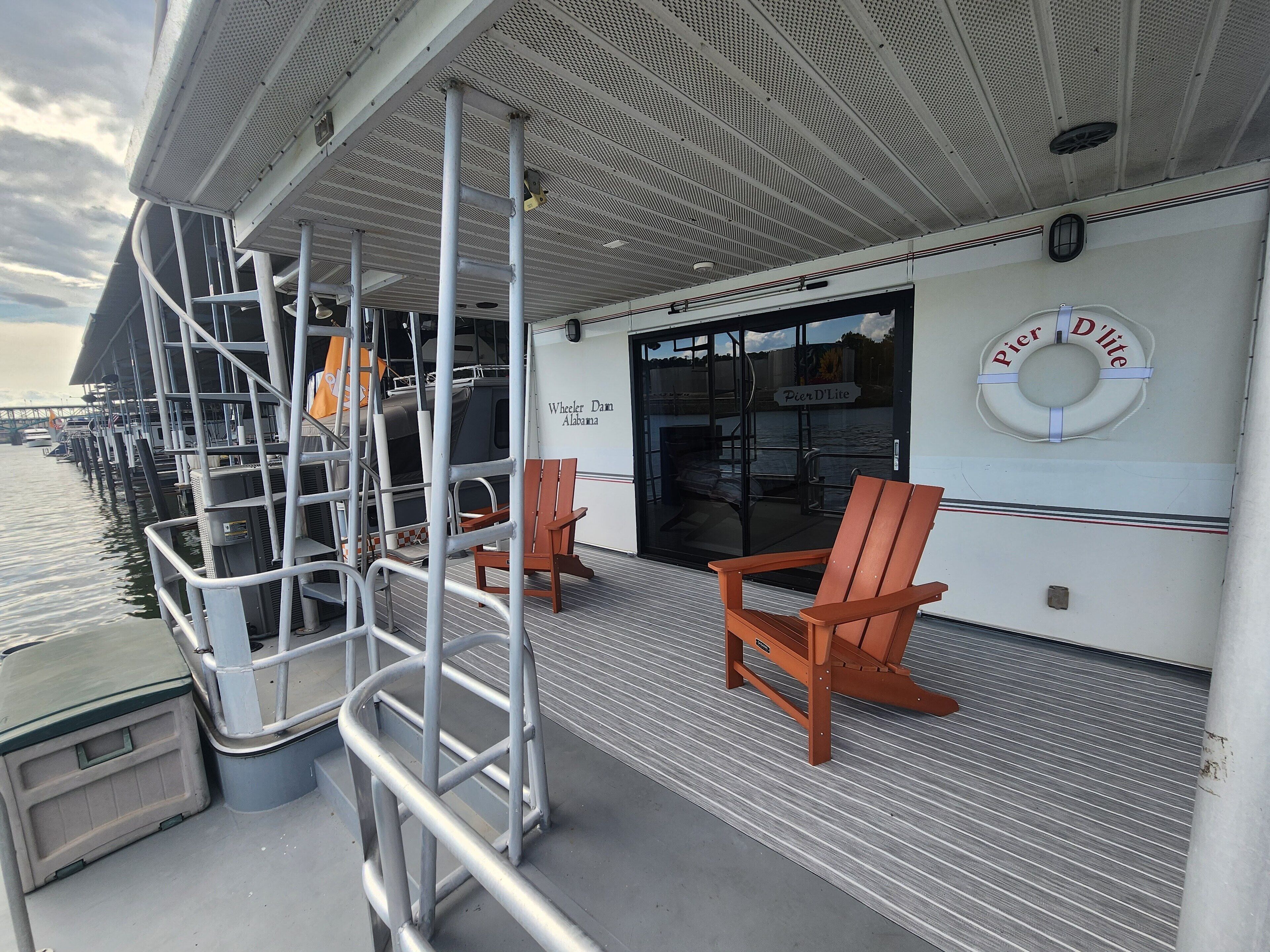 A deck with metal railings, two wooden chairs, and a sign reading "Pier D'Lite."