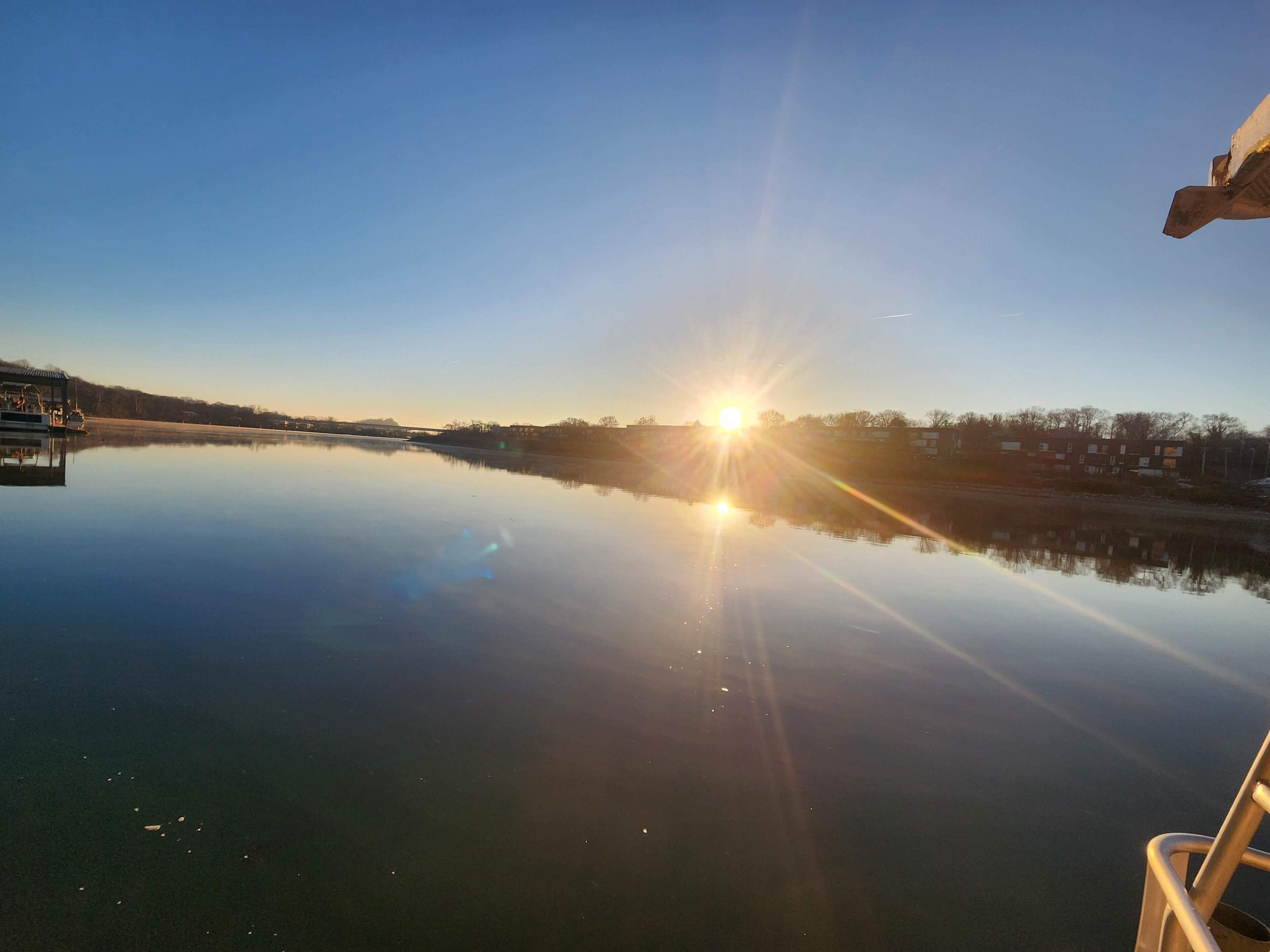 Un lago tranquilo con un reflejo claro del sol y edificios circundantes.