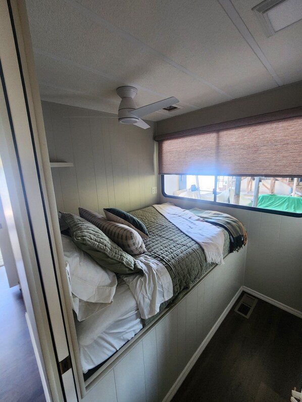 A small, single-bed room with a window, a ceiling fan, and a partial view of a door.