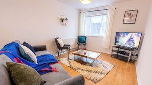 Una sala de estar con sofá, sillones, una mesa de centro, televisor y ventana con cortinas.