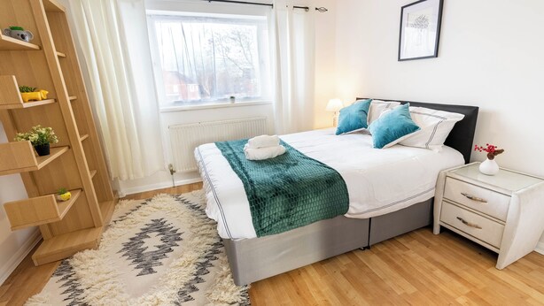 Un dormitorio con cama, mesitas de noche, ventana, radiador y una estantería empotrada de madera.