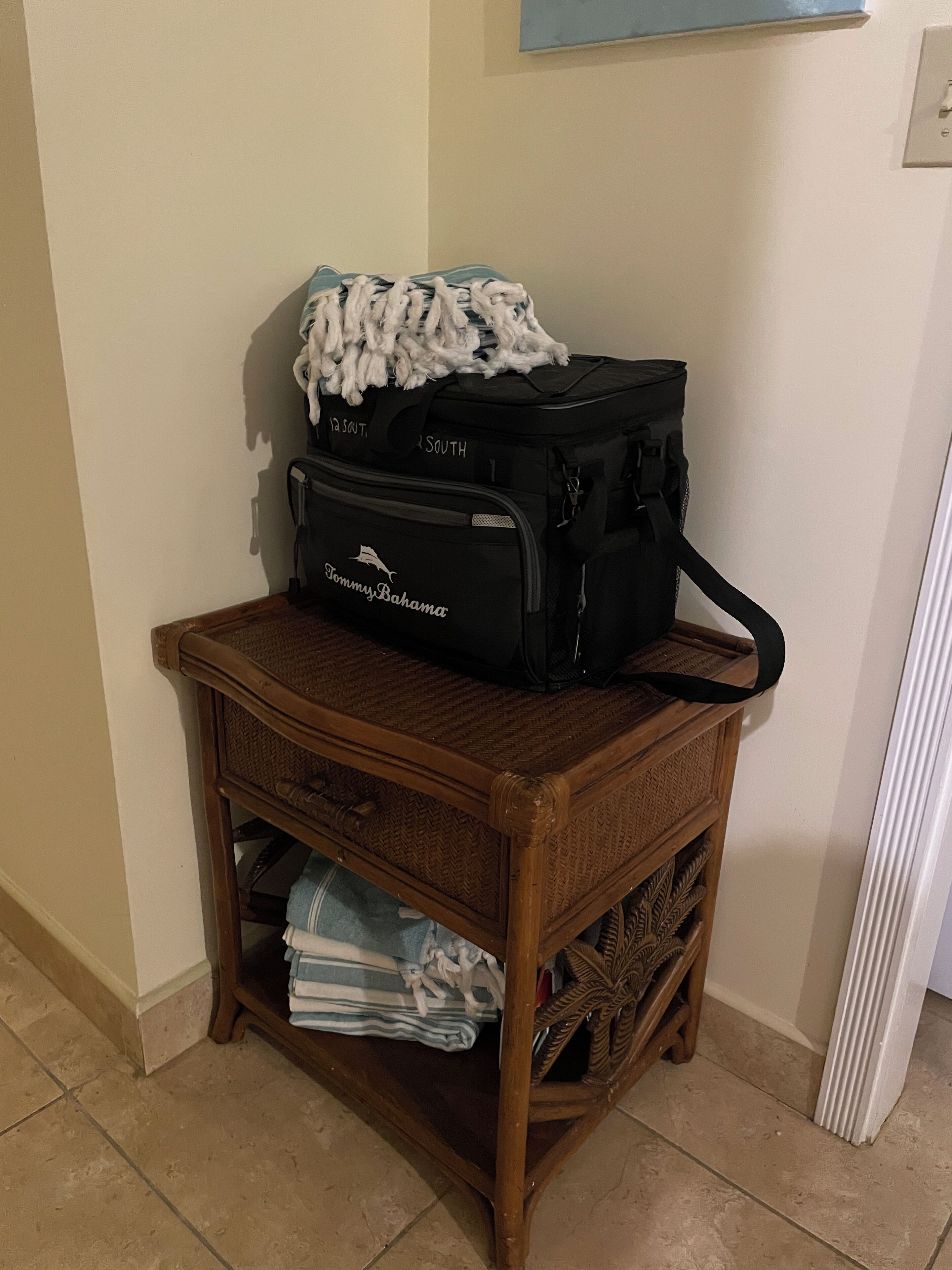 A wooden side table with a black suitcase and a blue and white striped towel on it.