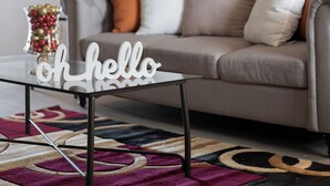 Een moderne woonkamer met een glazen salontafel, een bank met meerdere kussens, een lamp en een decoratief bord met de tekst 'hello'.