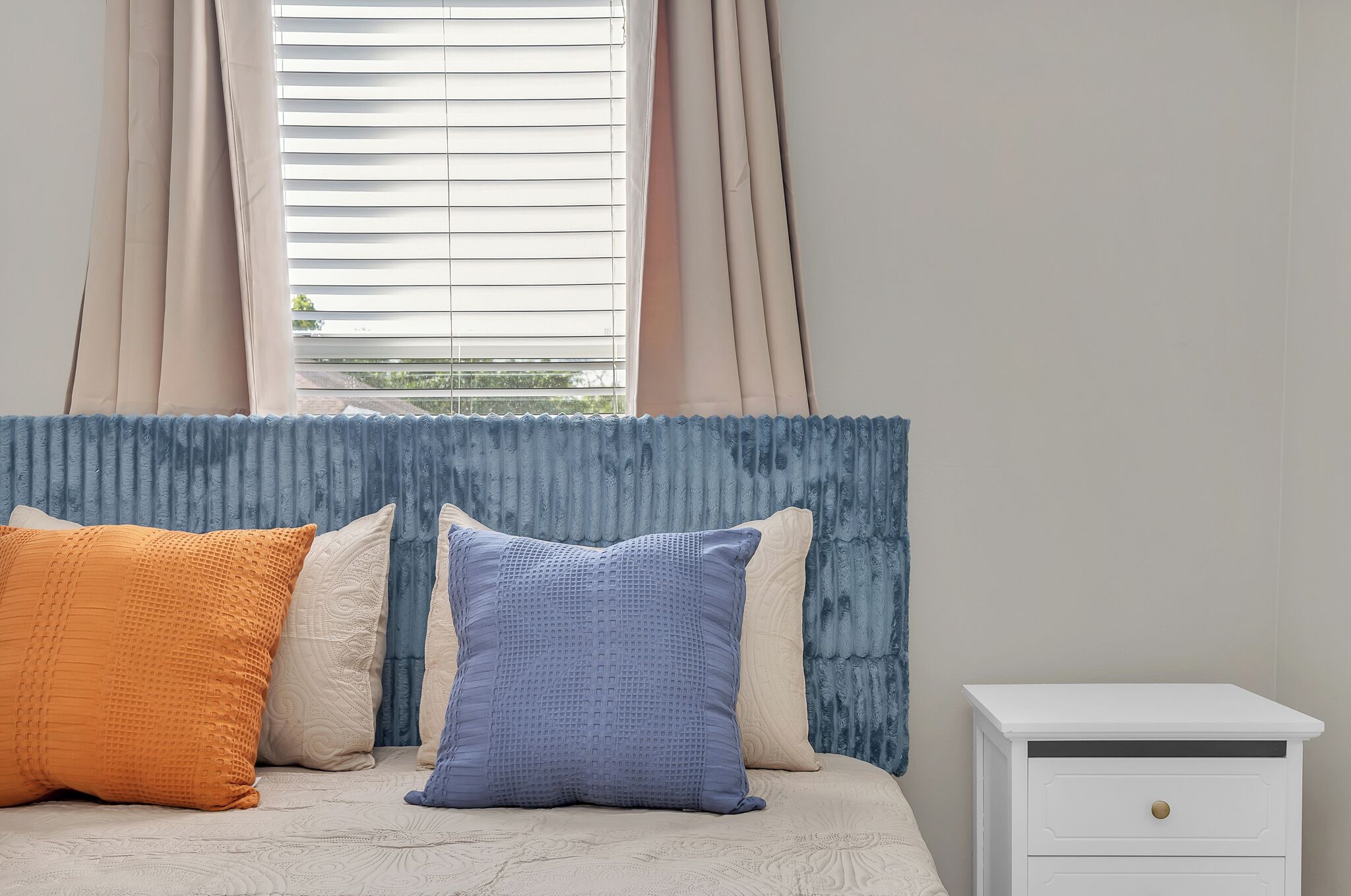 Una camera da letto con un letto, cuscini, un comodino e una finestra con tende.
