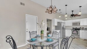 Een moderne keuken met witte kasten, roestvrijstalen apparatuur en een eethoek met een glazen tafel en metalen stoelen.