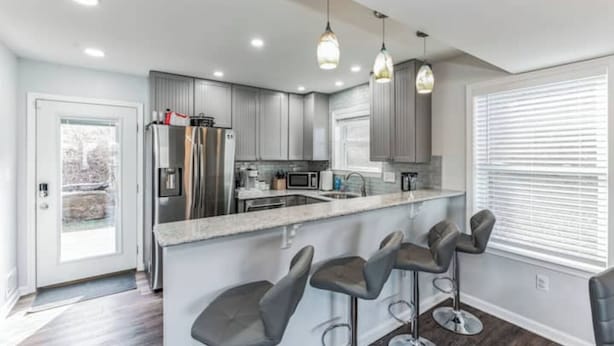 A modern kitchen with grey cabinets, stainless steel appliances, and a bar area with stools. - Mountain Ferry Landing - Riverfront Access (Charles Town)