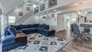 A spacious living room with a large sectional sofa, a patterned rug, and a staircase leading to an upper level. - Mountain Ferry Landing - Riverfront Access (Charles Town)