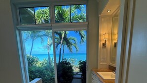 Ein Flur mit Blick auf eine tropische Landschaft durch große Fenster, der zu einem Badezimmer mit Waschbecken und Schränken führt.