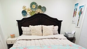 Una camera da letto con una struttura letto in legno scuro, una coperta trapuntata con motivo marino, un piatto decorativo appeso al muro e un comodino con una lampada.
