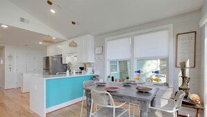 Una cucina moderna con mobili bianchi, un'isola centrale e un'area pranzo con sedie in vimini.