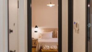 Un couloir d’hôtel menant à une chambre avec un lit, une table de chevet et un luminaire suspendu.