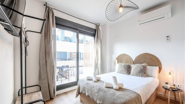 Moderni hotellihuone, jossa on suuri sänky, parveke, jolta on näkymä, riippuvalaisin ja ilmastointilaite.