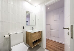 A modern bathroom with a white toilet, a wooden vanity with a sink, and a mirror.