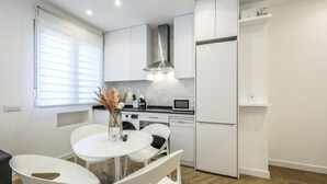 A modern kitchen with white cabinetry, a built-in oven, microwave, and dishwasher. There is a dining table with chairs and a vase of dried flowers. - Urban Tranquility in Madrid with Modern Comforts (Madrid)