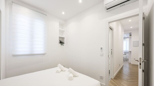 A modern bedroom with a large bed, a small window, and an air conditioning unit. - Urban Tranquility in Madrid with Modern Comforts (Madrid)
